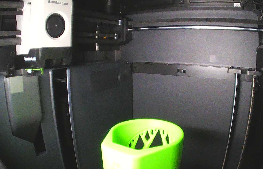 Chamber camera view of a Bambu Lab printer with a finished green print still on the build plate.